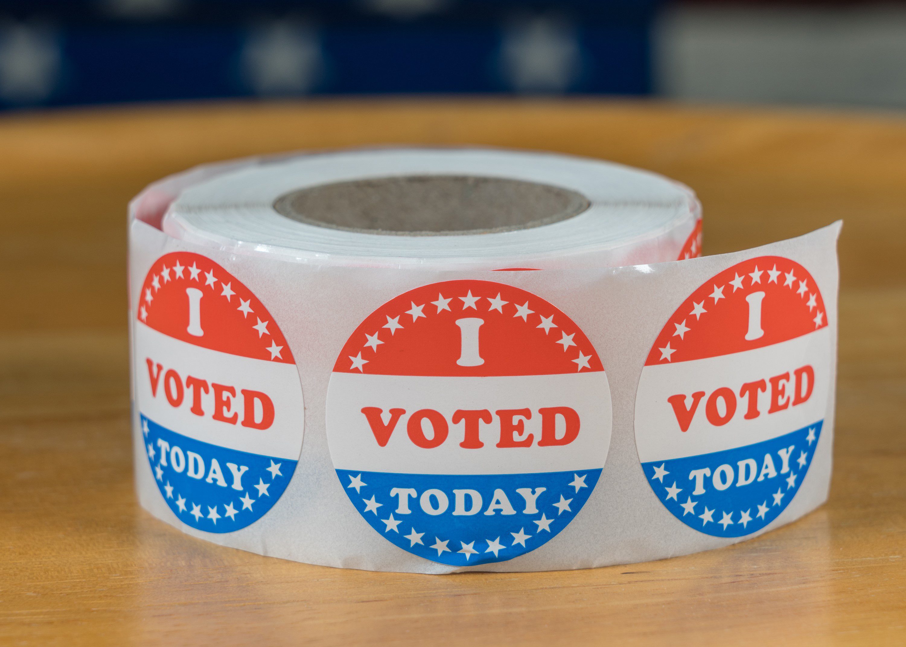Large roll of I Voted Today stickers ready for voters in the US elections with flag in background